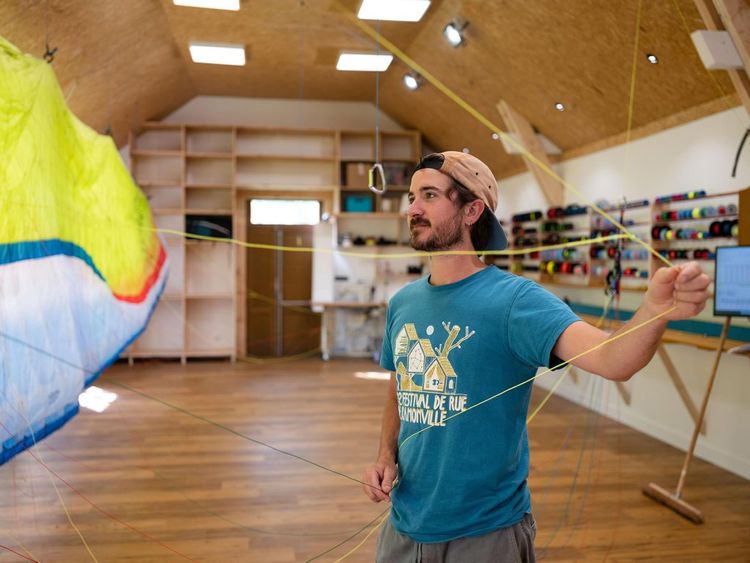 Lucas dans l'atelier en train de tirer sur les cordes d'une voile en réparation